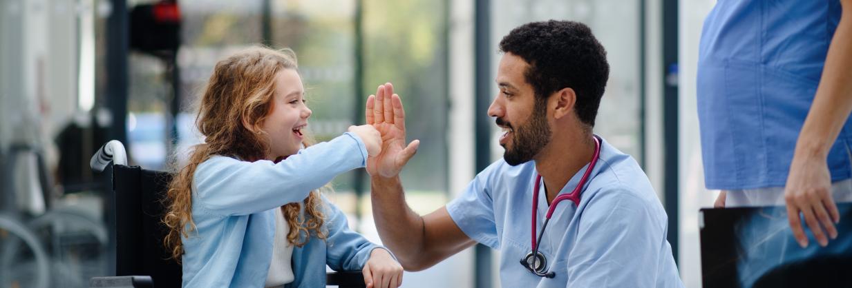 Nursing giving a young girl in a wheelchair a high five.