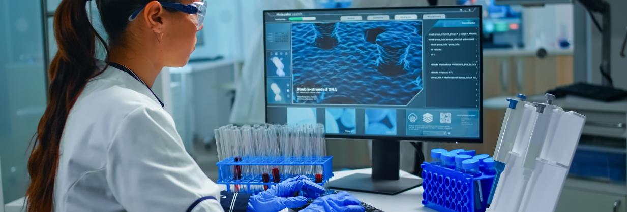 Laboratory technician entering data, while reviewing information on a monitor.