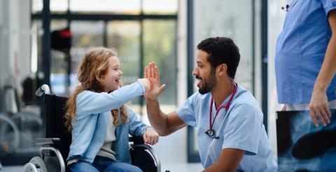 Nursing giving a young girl in a wheelchair a high five.